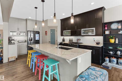 Spacious kitchen featuring a large island with a stone countertop, pendant lighting, two-tone cabinetry, a tile backsplash, and wood-finish flooring - 97 Astoria Point(E), Devon, AB - Indoor Photo Showing Kitchen With Upgraded Kitchen