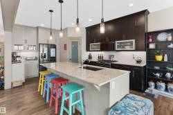 Spacious kitchen featuring a large island with a stone countertop, pendant lighting, two-tone cabinetry, a tile backsplash, and wood-finish flooring - 