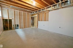 Unfinished basement space featuring exposed wood joists, concrete flooring, and partial drywall installation - 
