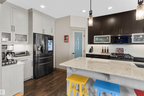 Modern kitchen featuring a large central island with a light-toned countertop, contrasting dark and light cabinetry, a built-in oven range, and wood-finish flooring - 97 Astoria Point(E), Devon, AB - Indoor Photo Showing Kitchen With Upgraded Kitchen