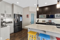 Modern kitchen featuring a large central island with a light-toned countertop, contrasting dark and light cabinetry, a built-in oven range, and wood-finish flooring - 