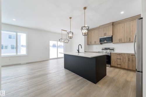 Spacious kitchen featuring a dark island with a light countertop, wood-finish cabinetry, stainless steel appliances, and a white subway tile backsplash - 162 Caldeon Crescent, Spruce Grove, AB - Indoor Photo Showing Kitchen With Upgraded Kitchen