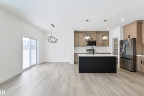 Modern kitchen featuring light wood-finish cabinetry, stainless steel appliances, and a central island with a contrasting black base and white countertop - 162 Caldeon Crescent, Spruce Grove, AB - Indoor Photo Showing Kitchen With Upgraded Kitchen