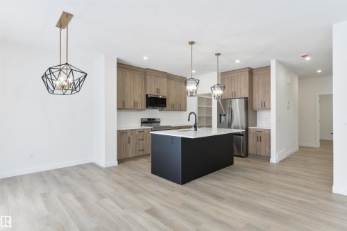 Open-concept kitchen featuring a dark island with a white countertop, stainless steel appliances, light wood-finish cabinetry, and contemporary pendant lighting - 162 Caldeon Crescent, Spruce Grove, AB - Indoor Photo Showing Kitchen With Upgraded Kitchen