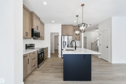 Modern kitchen featuring a central island with a white countertop and dark base, stainless steel appliances, wood-finish cabinetry, and contemporary pendant lighting - 162 Caldeon Crescent, Spruce Grove, AB - Indoor Photo Showing Kitchen With Upgraded Kitchen