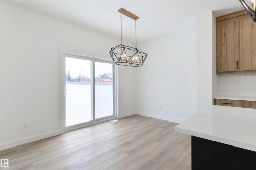 Open-concept dining area featuring light wood-finish flooring, a geometric black and gold chandelier, and a sliding glass door - 162 Caldeon Crescent, Spruce Grove, AB - Indoor Photo Showing Other Room