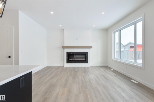 Spacious living area featuring light wood-finish flooring, a contemporary fireplace with a wood mantle, recessed lighting, and a large window - 162 Caldeon Crescent, Spruce Grove, AB - Indoor Photo Showing Living Room With Fireplace