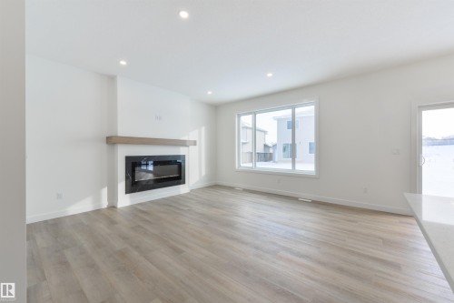 Bright living area featuring wood-finish flooring, a contemporary fireplace with a black surround and wood mantel, recessed lighting, and a large window - 162 Caldeon Crescent, Spruce Grove, AB - Indoor Photo Showing Living Room With Fireplace