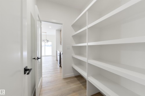 Walk-in pantry featuring extensive built-in shelving, light wood-finish flooring, and a frosted glass panel door with matte black hardware - 162 Caldeon Crescent, Spruce Grove, AB - Indoor With Storage