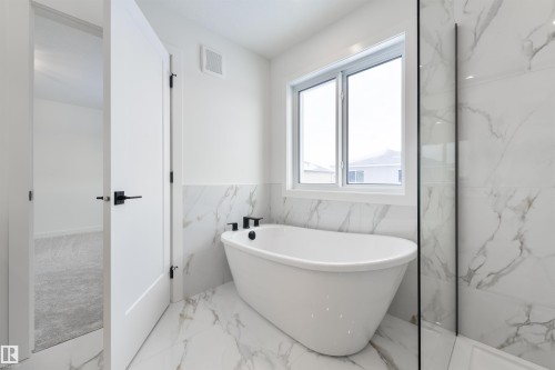 Freestanding soaking tub with black fixtures, set against large format marble-look tile flooring and wainscoting - 162 Caldeon Crescent, Spruce Grove, AB - Indoor Photo Showing Bathroom
