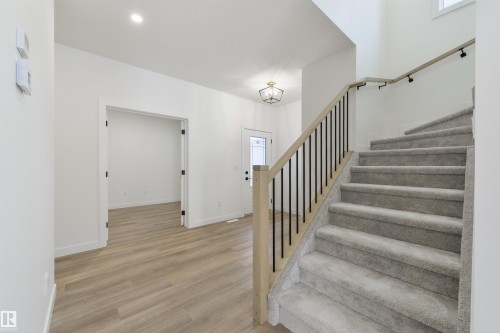 Foyer featuring light wood-finish flooring, a carpeted staircase with wood and metal railings, an open doorway, and a ceiling-mounted light fixture - 162 Caldeon Crescent, Spruce Grove, AB - Indoor Photo Showing Other Room