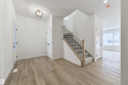 Entry foyer featuring wood-finish flooring, a modern geometric flush-mount light fixture, a staircase with light wood newel posts and black metal spindles, and white paneled doors - 162 Caldeon Crescent, Spruce Grove, AB - Indoor Photo Showing Other Room