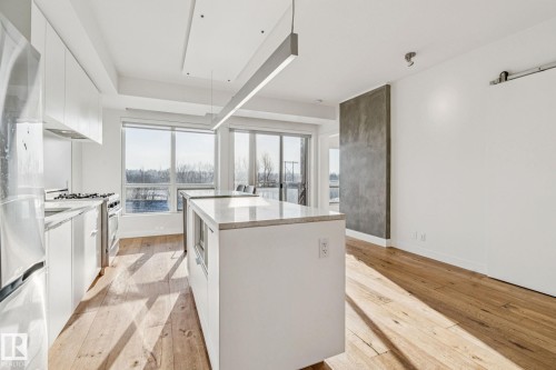 The kitchen features hardwood floors, white cabinetry, a kitchen island with a stone countertop, and stainless steel appliances - #321 63 Inglewood Park, Calgary, AB - Indoor Photo Showing Kitchen