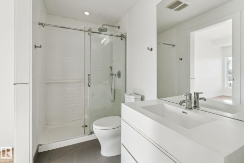 Bathroom featuring a glass-enclosed shower, a wall-mounted vanity with an integrated sink, and a large mirror - #321 63 Inglewood Park, Calgary, AB - Indoor Photo Showing Bathroom