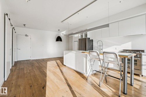 The property features hardwood floors, a kitchen island with seating, white cabinetry, and stainless steel appliances - #321 63 Inglewood Park, Calgary, AB - Indoor