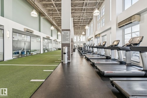 Fitness area featuring a row of treadmills, a green turf track, high ceilings with exposed beams, and large windows providing natural light - #321 63 Inglewood Park, Calgary, AB - Indoor Photo Showing Gym Room