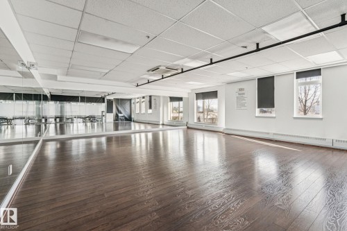 The property features expansive hardwood floors, large mirrored walls, and multiple windows with roller blinds providing views of the outdoors - #321 63 Inglewood Park, Calgary, AB - Indoor