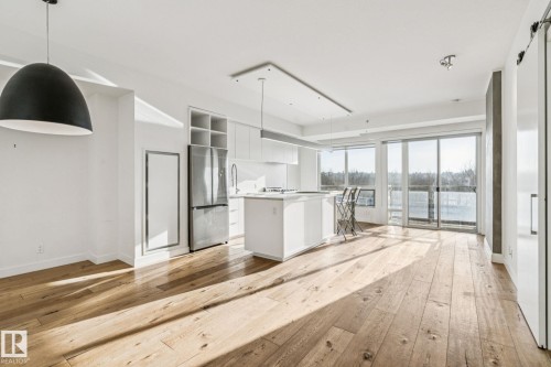 This bright living space features light-toned hardwood floors, a kitchen island with seating, a stainless steel refrigerator, and sliding glass doors leading to an outdoor area - #321 63 Inglewood Park, Calgary, AB - Indoor