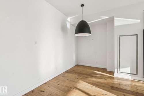 This space features light hardwood floors, white walls, and a modern black pendant light fixture - #321 63 Inglewood Park, Calgary, AB - Indoor Photo Showing Other Room