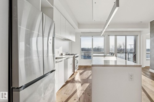 Kitchen featuring white cabinetry, stainless steel appliances, a kitchen island with a light-colored countertop, and hardwood floors - #321 63 Inglewood Park, Calgary, AB - Indoor Photo Showing Kitchen