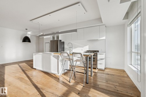 Open-concept living area featuring light-colored hardwood flooring, a contemporary kitchen with white cabinetry, a kitchen island, and stainless steel appliances, all complemented by natural light from the large window - #321 63 Inglewood Park, Calgary, AB - Indoor Photo Showing Other Room