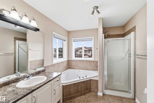 Bathroom featuring a built-in corner tub with tiled surround, a separate glass-enclosed shower, a single vanity with an integrated sink and stone-look countertop, and an overhead vanity light fixture - 16412 60 Street, Edmonton, AB - Indoor Photo Showing Bathroom