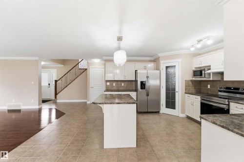 Modern kitchen featuring white cabinetry, stainless steel appliances, a center island with bar seating, tile flooring, and a tile backsplash - 16412 60 Street, Edmonton, AB - Indoor Photo Showing Kitchen