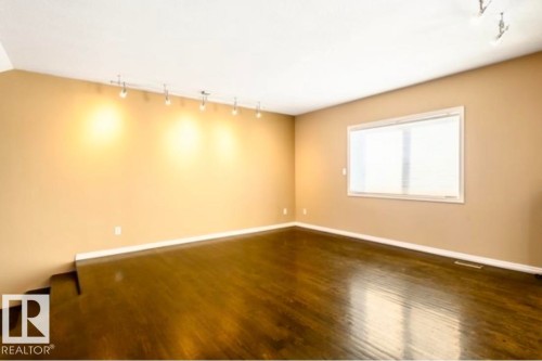 Spacious room featuring dark wood-finish flooring, neutral wall paint, a large window with horizontal blinds, and track lighting fixtures - 18633 122 Avenue, Edmonton, AB - Indoor Photo Showing Other Room