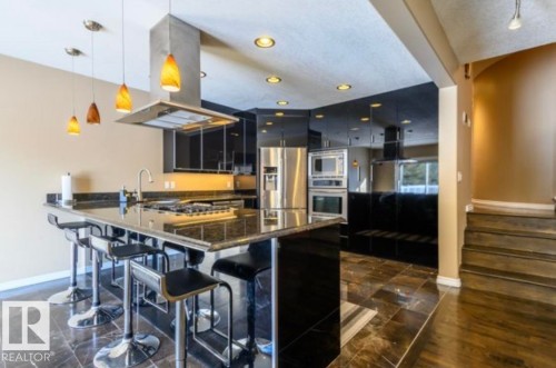 Gourmet kitchen featuring a granite countertop island with integrated cooktop, stainless steel appliances, recessed lighting, and rich dark cabinetry - 18633 122 Avenue, Edmonton, AB - Indoor