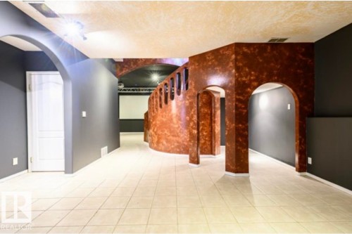 Spacious interior featuring a projector screen, arched walkways, track lighting, light-toned tiled flooring, and dark-painted walls - 18633 122 Avenue, Edmonton, AB - Indoor Photo Showing Other Room