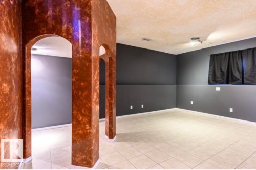 Room featuring arched passageways with textured pillars, neutral-toned tile flooring, and dark-painted walls - 18633 122 Avenue, Edmonton, AB - Indoor Photo Showing Other Room