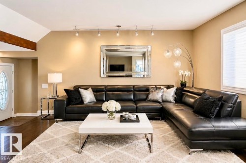 Virtually staged. Spacious living area featuring track lighting, a large window with privacy blinds, wood-finish flooring, and a decorative front entry door with an oval glass insert - 18633 122 Avenue, Edmonton, AB - Indoor Photo Showing Living Room