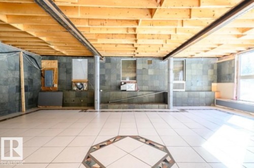Spacious room featuring light-toned tile flooring with a central mosaic detail, exposed wood ceiling joists, and dark stone-finish wall tiling - 18633 122 Avenue, Edmonton, AB - Indoor Photo Showing Other Room