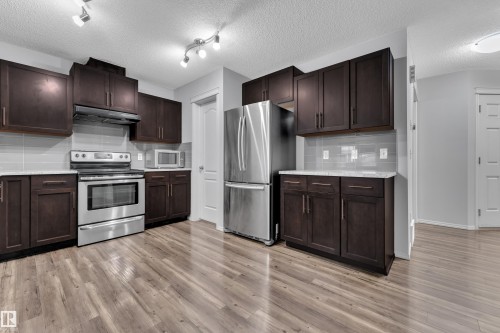 Kitchen featuring rich wood cabinetry, stainless steel appliances, light-toned backsplash, and wood-finish flooring - 718 177 Street, Edmonton, AB - Indoor Photo Showing Kitchen