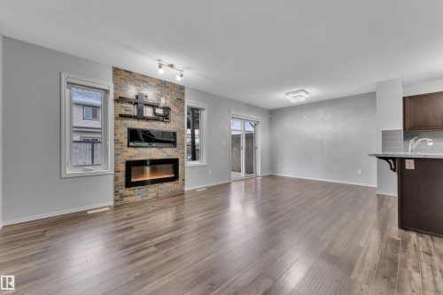 Spacious living area featuring light wood-finish flooring, a contemporary electric fireplace with a stacked stone facade, and a built-in media center - 718 177 Street, Edmonton, AB - Indoor With Fireplace