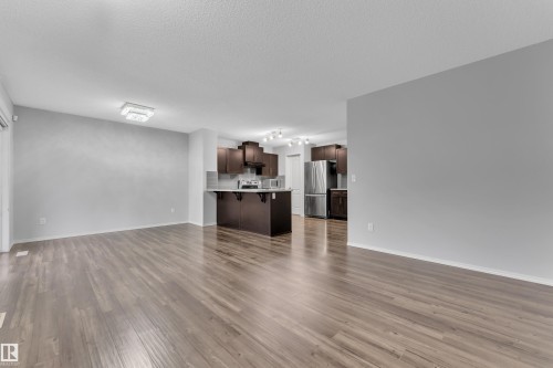 Open-concept living space featuring wood-finish flooring, a contemporary ceiling light fixture, and a kitchen with dark cabinetry, stainless steel appliances, and a breakfast bar - 718 177 Street, Edmonton, AB - Indoor Photo Showing Living Room
