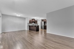 Open-concept living space featuring wood-finish flooring, a contemporary ceiling light fixture, and a kitchen with dark cabinetry, stainless steel appliances, and a breakfast bar - 