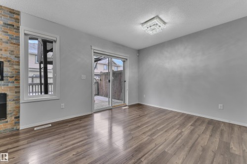 Spacious room featuring wood-finish flooring, a contemporary ceiling light fixture, a floor-to-ceiling multi-color brick accent wall with a built-in fireplace, and a sliding glass door leading to an outdoor space - 718 177 Street, Edmonton, AB - Indoor Photo Showing Other Room With Fireplace
