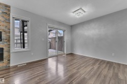Spacious room featuring wood-finish flooring, a contemporary ceiling light fixture, a floor-to-ceiling multi-color brick accent wall with a built-in fireplace, and a sliding glass door leading to an outdoor space - 