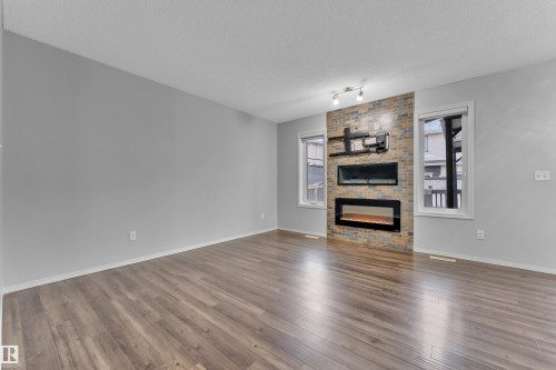 Spacious room featuring wood-finish flooring, light grey walls, and an accent wall with a built-in linear electric fireplace - 718 177 Street, Edmonton, AB - Indoor Photo Showing Living Room
