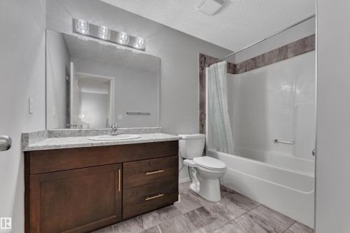Bathroom featuring a wood-finish vanity with a light-colored countertop, integrated sink, and an expansive wall mirror - 718 177 Street, Edmonton, AB - Indoor Photo Showing Bathroom