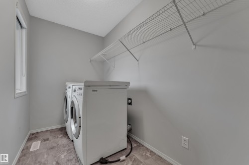 Dedicated laundry area featuring a window, light gray walls, a built-in wire shelf, and stone-finish flooring - 718 177 Street, Edmonton, AB - Indoor Photo Showing Laundry Room