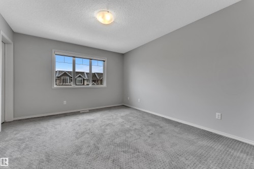 Spacious room featuring neutral gray walls, gray patterned carpet, and a large window with white trim - 718 177 Street, Edmonton, AB - Indoor Photo Showing Other Room