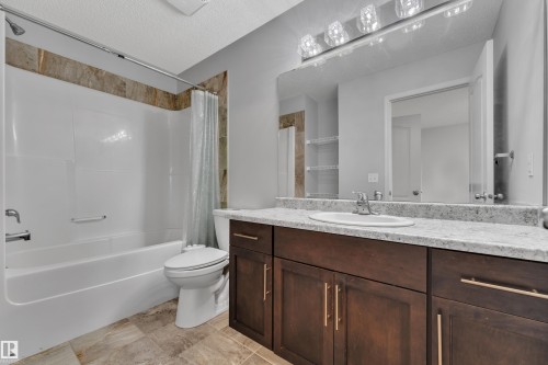Bathroom featuring a dark wood-finish vanity with a light speckled countertop, an integrated sink, and a large mirror with a multi-bulb light fixture - 718 177 Street, Edmonton, AB - Indoor Photo Showing Bathroom