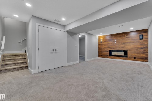 Spacious lower-level area featuring a modern linear fireplace set into a wood-finish accent wall - 718 177 Street, Edmonton, AB - Indoor Photo Showing Other Room