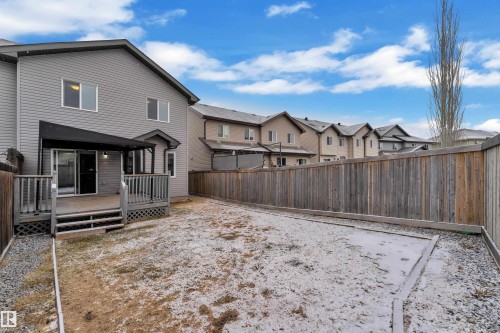 Expansive backyard featuring a privacy fence, wood-finish deck with railing, sliding glass door access, exterior lighting, and a partial awning - 718 177 Street, Edmonton, AB - Outdoor