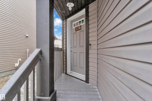Covered entry with dark wood-finish decking and railing, light gray siding, and a paneled entry door with transom window - 718 177 Street, Edmonton, AB - Outdoor With Exterior