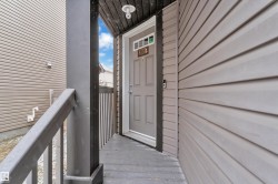 Covered entry with dark wood-finish decking and railing, light gray siding, and a paneled entry door with transom window - 