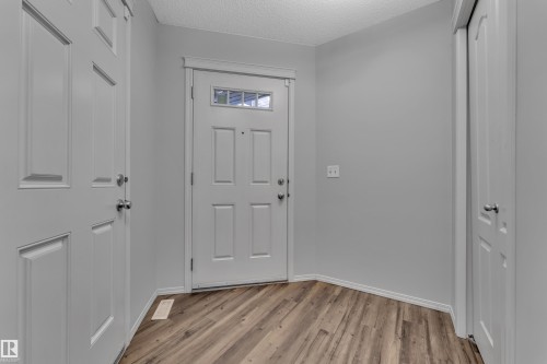 Entryway featuring wood-finish flooring, light gray walls, a white paneled door with a transom window, white baseboards, and two additional white paneled doors - 718 177 Street, Edmonton, AB - Indoor Photo Showing Other Room
