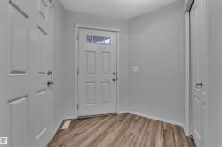 Entryway featuring wood-finish flooring, light gray walls, a white paneled door with a transom window, white baseboards, and two additional white paneled doors - 